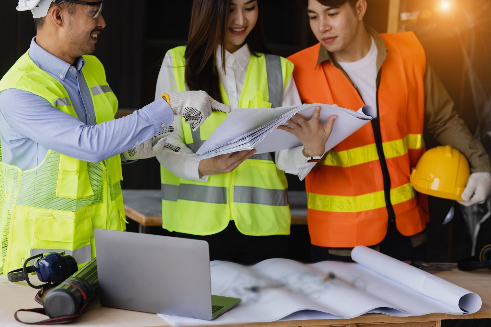 Three construction workers reviewing blueprints at a table, one pointing.