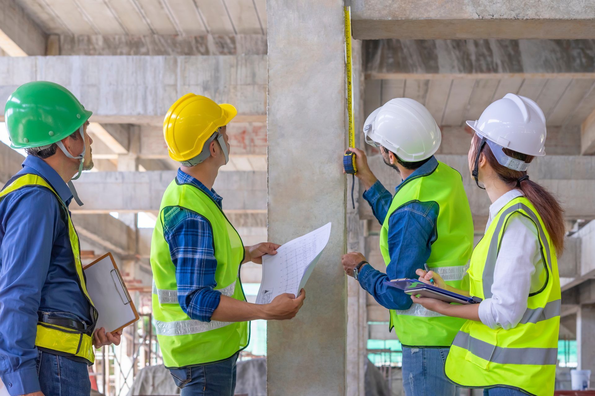 Construction workers measuring a concrete pillar on a building site.