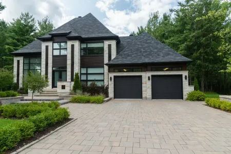 A modern two-story house with a stone facade, black garage doors, and a brick driveway.
