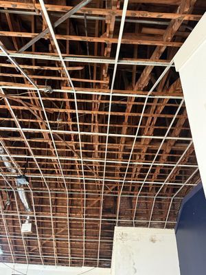 Wooden ceiling with white grid supports, wiring, and visible beams.