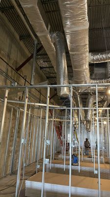 Construction site: Metal studs, ductwork wrapped in foil, workers, unfinished interior.