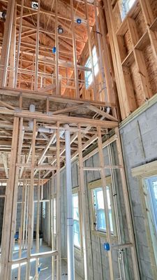 Wooden framing of a multi-story building under construction; plumbing and electrical work visible.