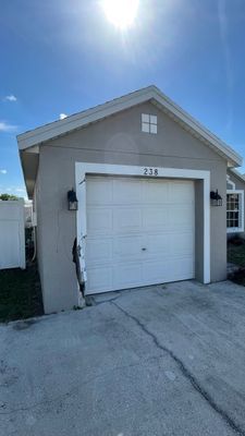 Garage with white door and light gray stucco exterior under a bright sunny sky.