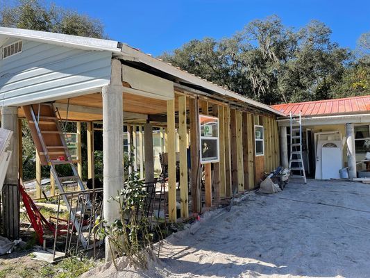 House exterior under construction; exposed wooden frame, metal roof, concrete pillars.