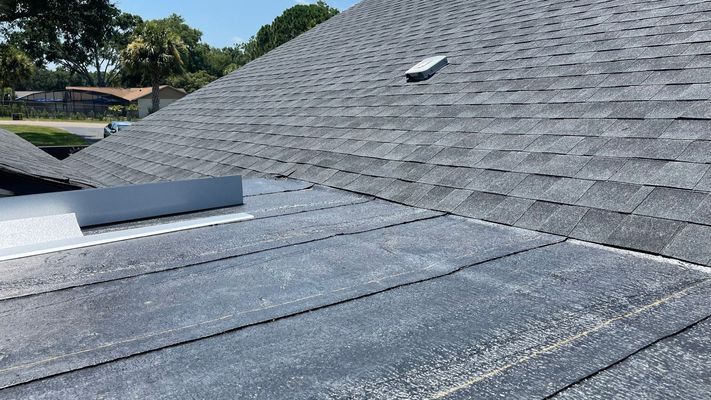 Gray asphalt shingle roof with a metal flashing and a roof vent on a sunny day.