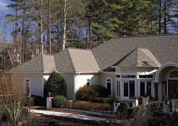 A large white house with a gray roof is surrounded by trees.