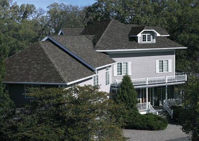 A large white house with a black roof is surrounded by trees