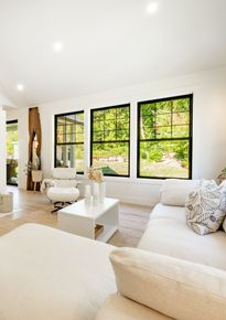 A living room with a couch , chair , coffee table and three windows.