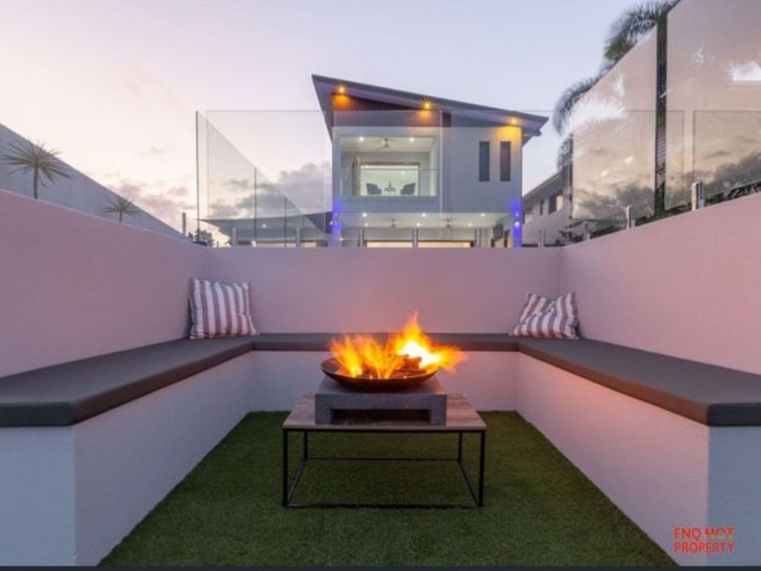 Modern patio with a central fire pit, built-in benches, and a house lit in the background at dusk