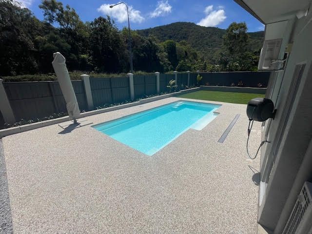 Backyard pool with turquoise water, pebble patio, fence, and hills under a blue sky