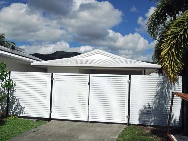 White house facade with a white gate and fence under a blue sky with clouds