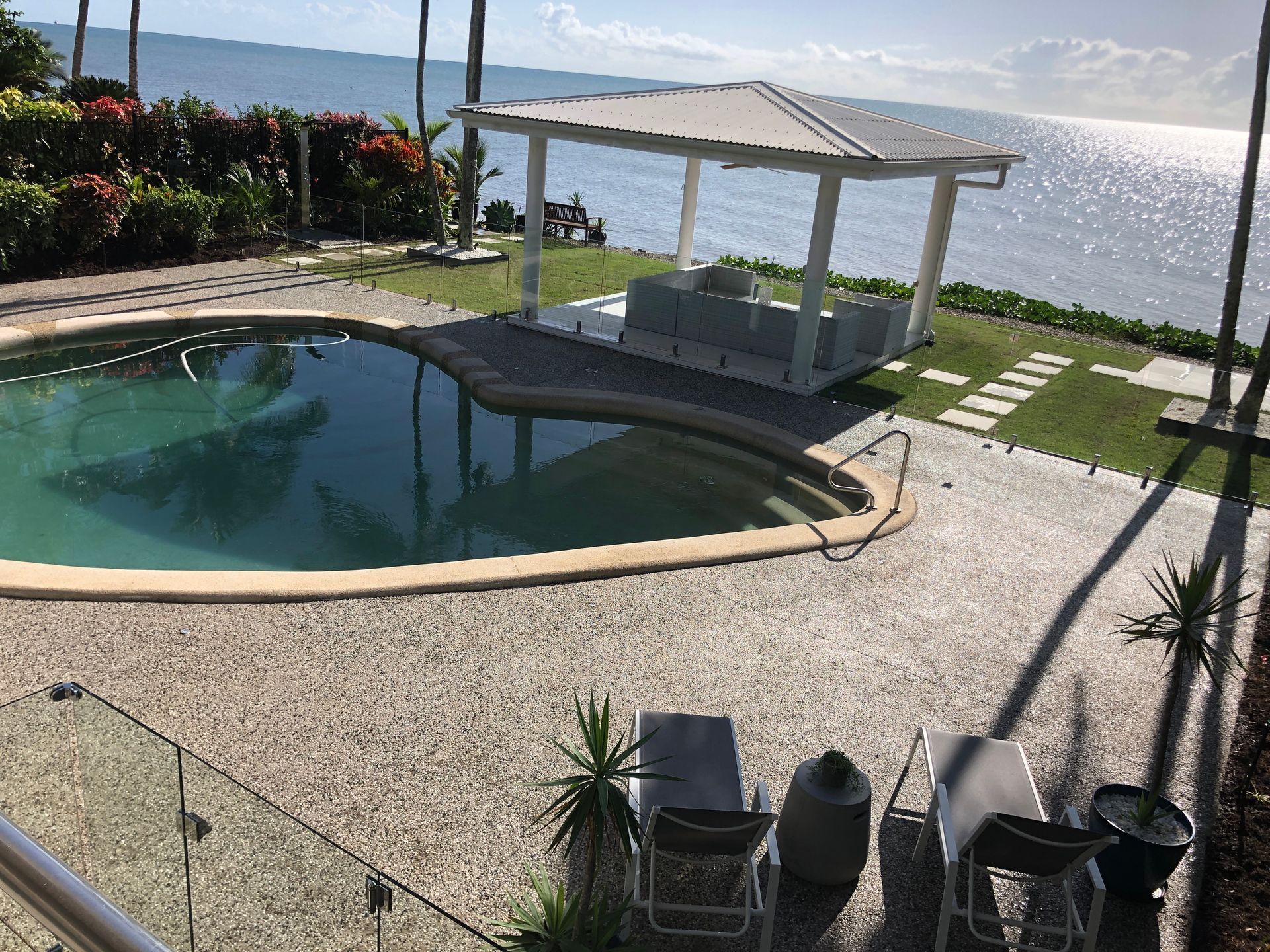 Backyard pool beside a white cabana overlooking sparkling water and a distant shoreline.