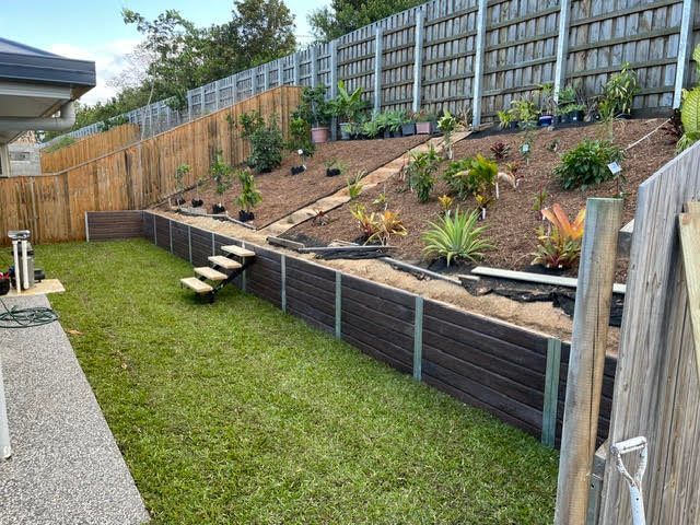 Backyard with sloped garden bed, retaining wall, steps, fence, and lawn