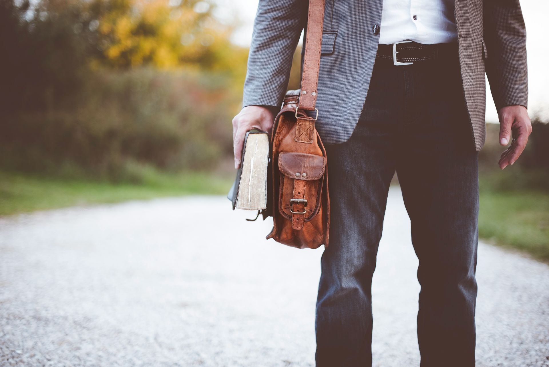 A man is walking down a road holding a book and a briefcase.