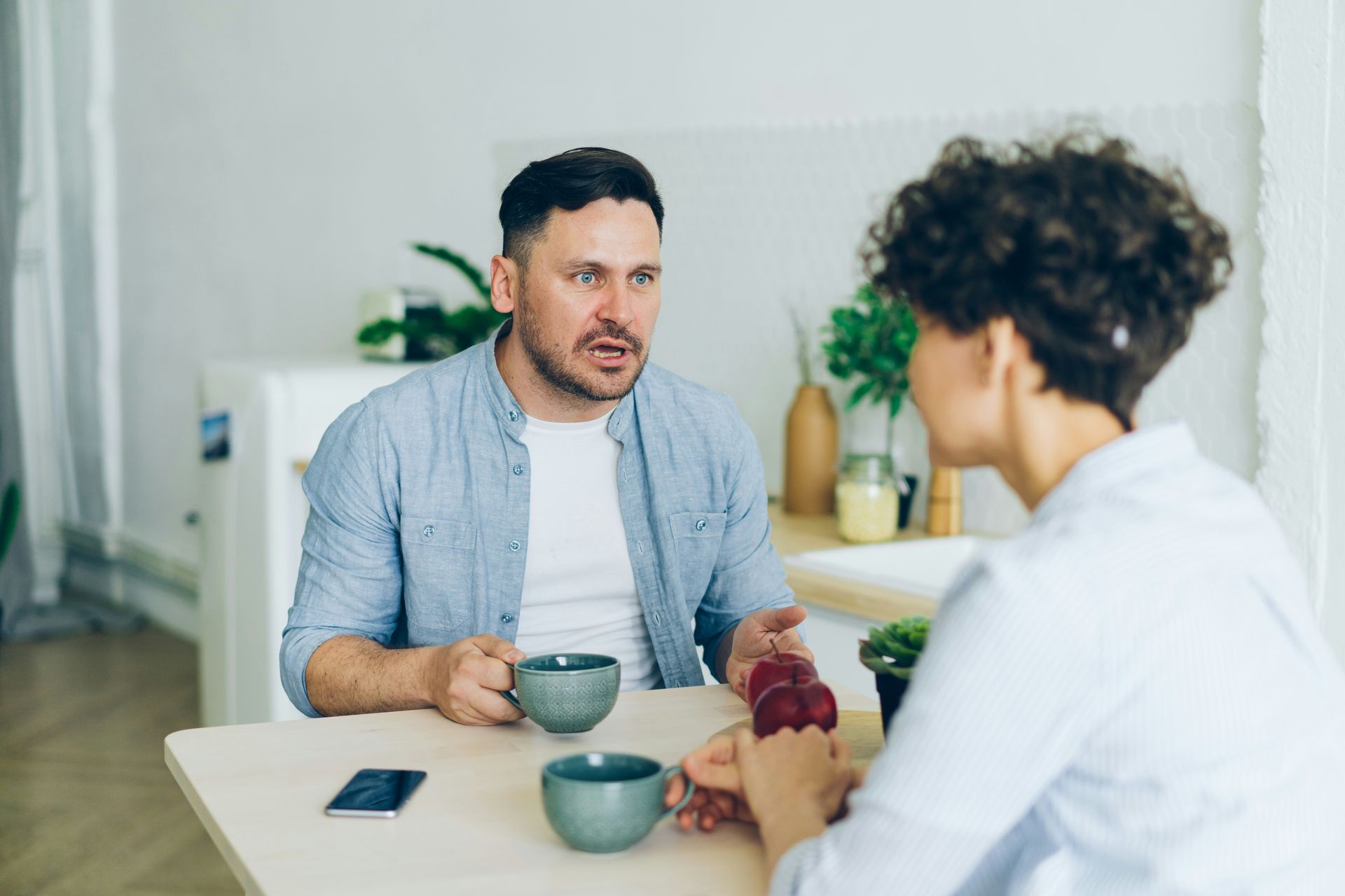 A man and a woman are sitting at a table drinking coffee and talking.