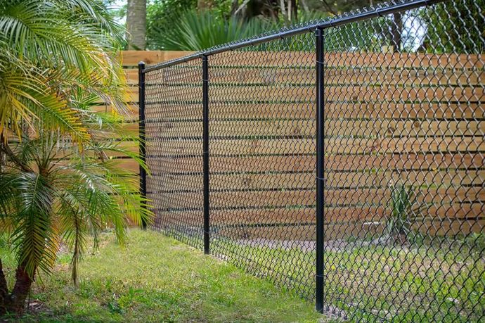 A chain link fence with a wooden fence behind it.