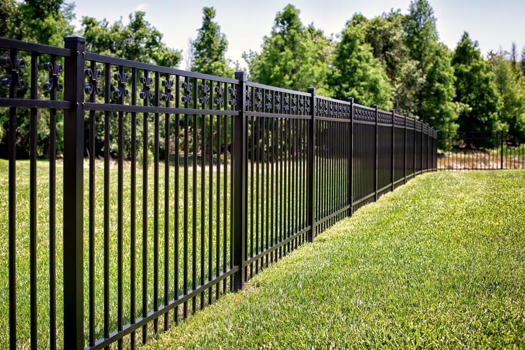A black metal fence surrounds a lush green field.