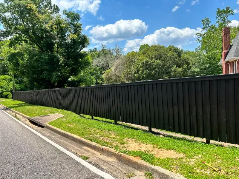 A long black fence along the side of a road next to a house.