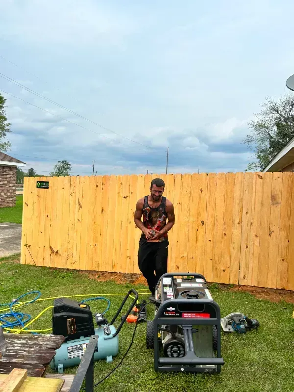 A man is standing in front of a wooden fence.