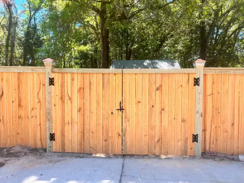A wooden fence with a gate is sitting on top of a concrete driveway.