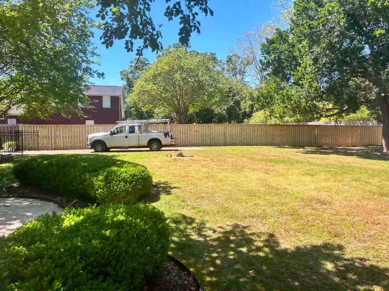 A white truck is parked in a grassy yard next to a wooden fence.