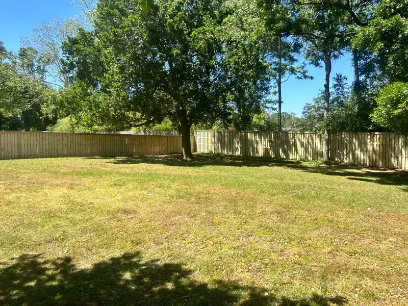 A large lawn with a wooden fence and trees in the background.
