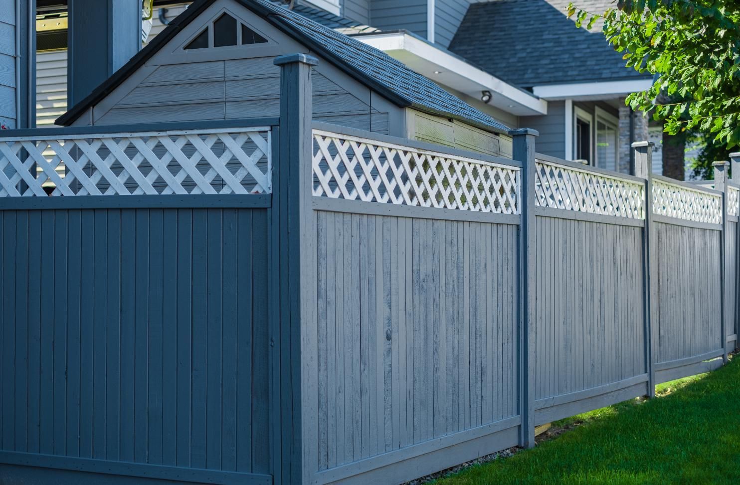 A wooden fence with a lattice design is in front of a house.