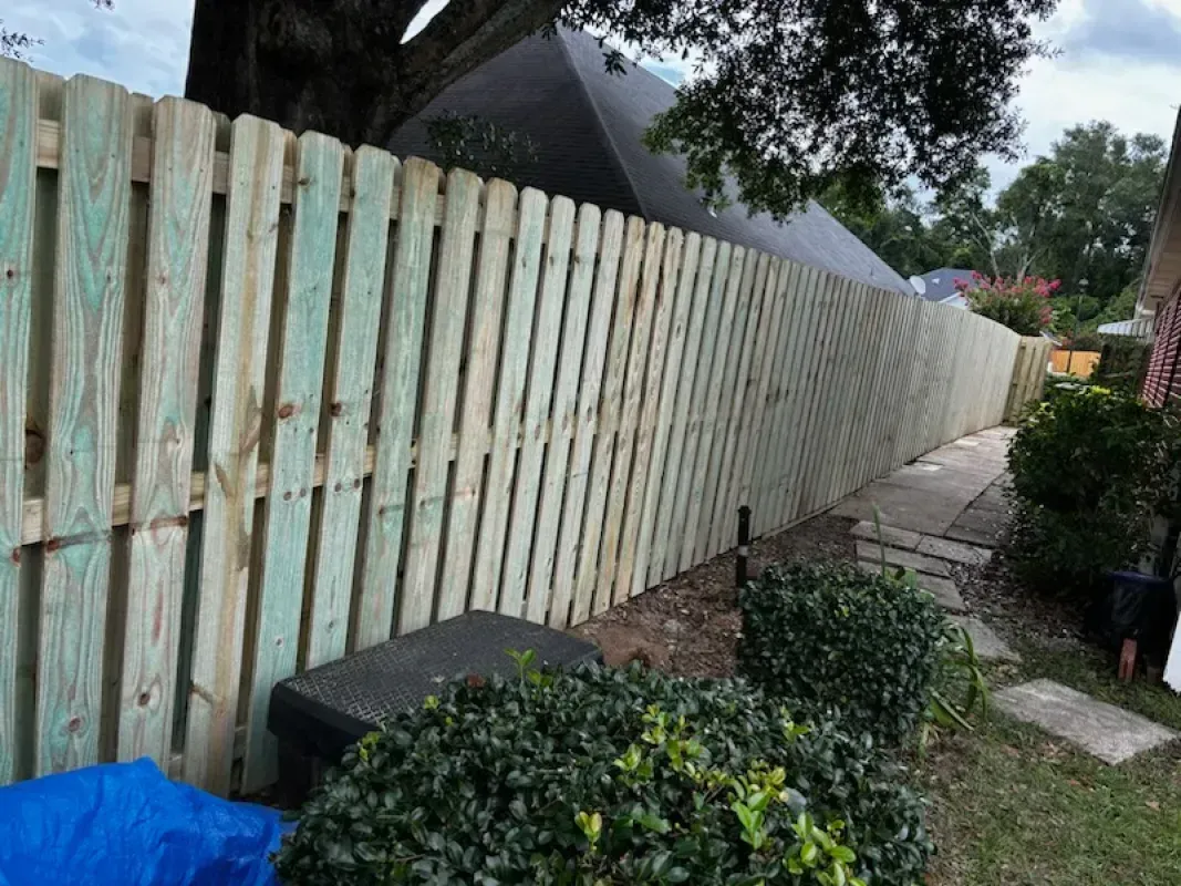 A wooden fence is sitting next to a sidewalk in a yard.
