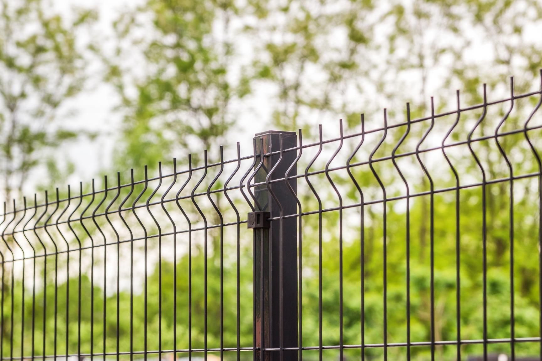 A close up of a wire fence with trees in the background.