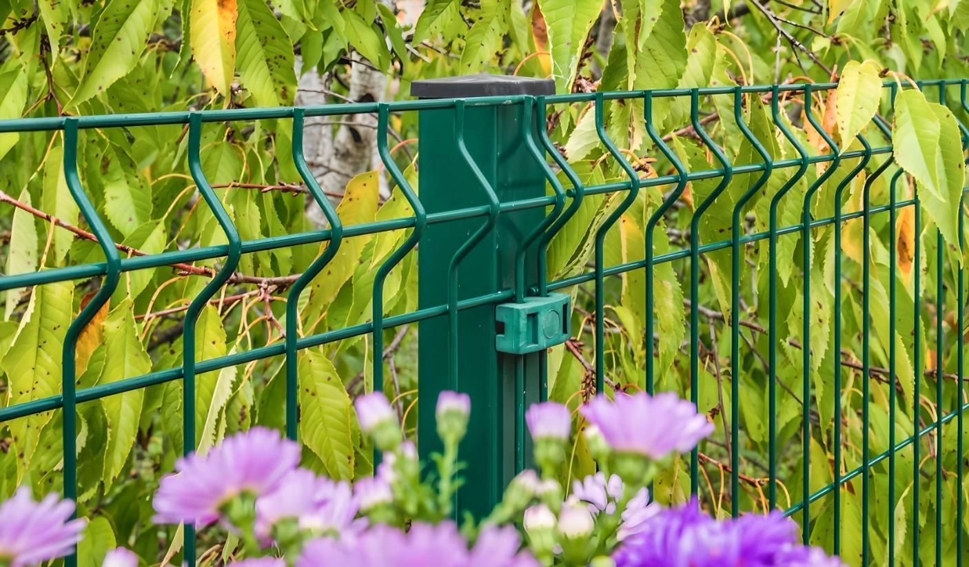 A green fence with purple flowers in front of it.