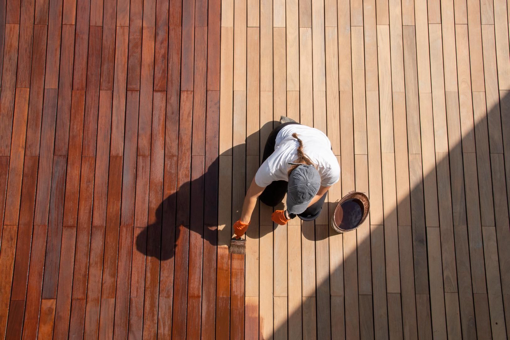A man is painting a wooden deck with a brush.