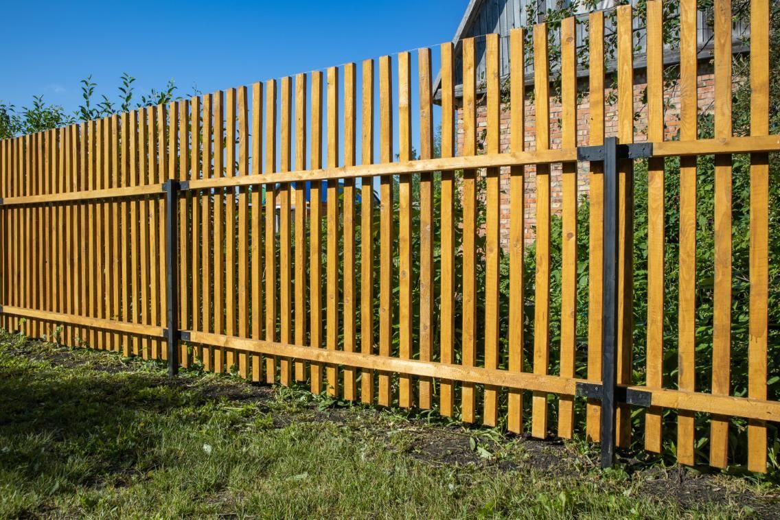 A wooden fence is surrounded by grass and trees in a yard.