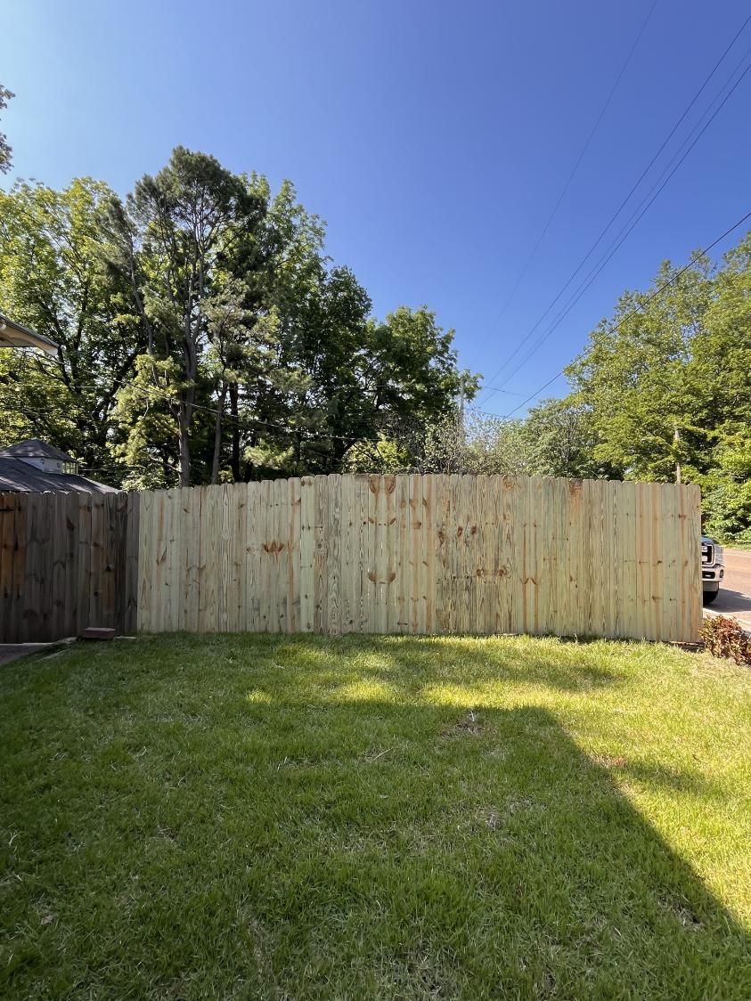 A wooden fence is in the middle of a lush green yard.