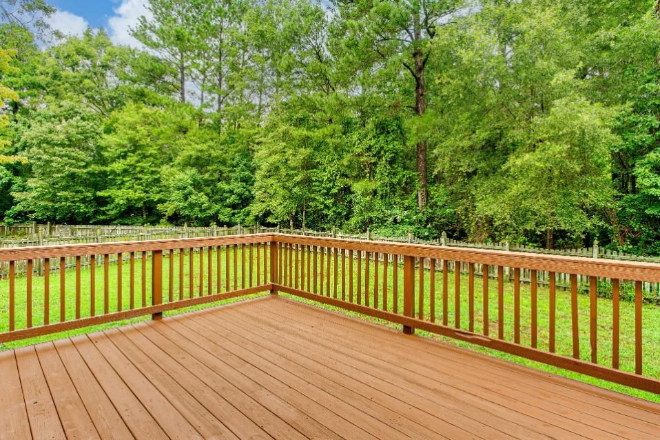 An empty wooden deck with a wooden railing overlooking a lush green field.