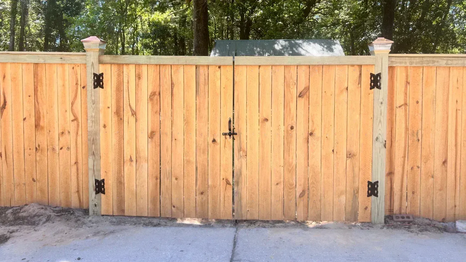 A wooden fence with a gate is sitting on top of a concrete driveway.