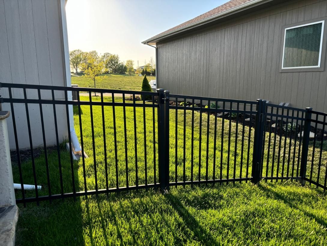 A black fence surrounds a lush green yard in front of a house.