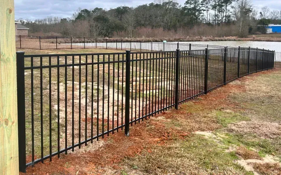 A black metal fence surrounds a grassy field next to a lake.