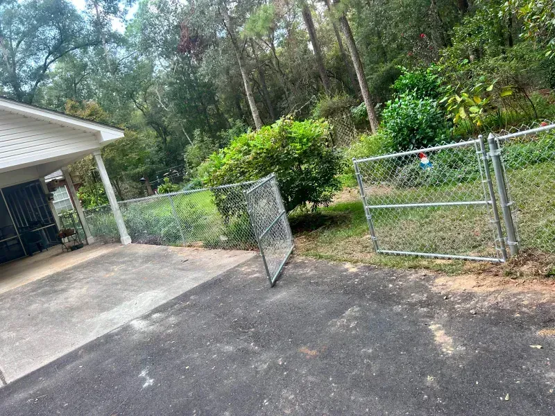 A chain link fence is sitting on the side of a road next to a house.