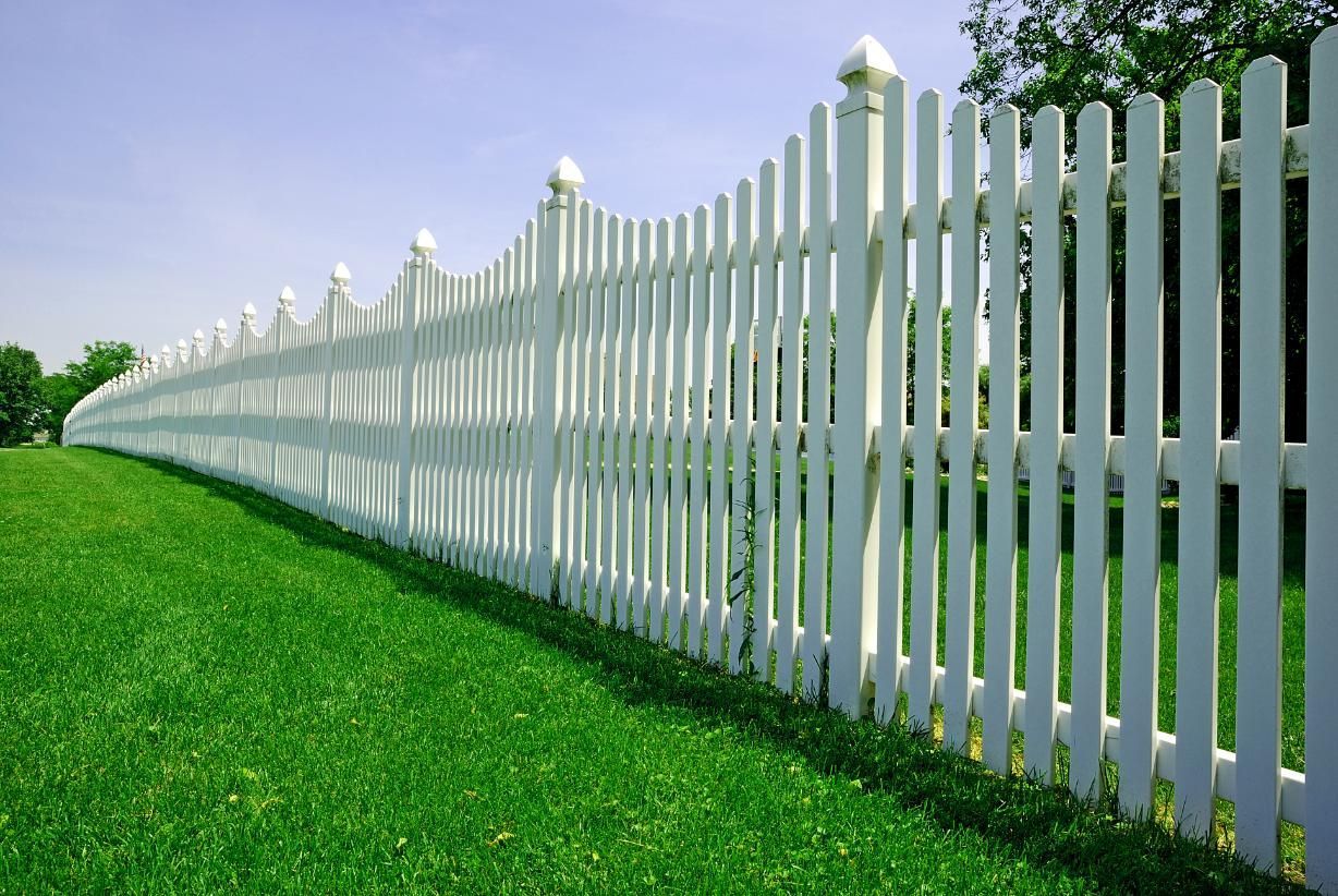 A long white picket fence surrounds a lush green field.