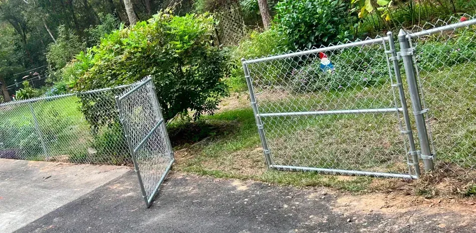 A chain link fence is broken in half on the side of a road.