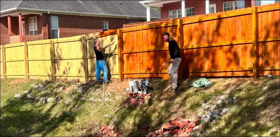 Two men are painting a wooden fence in front of a house.