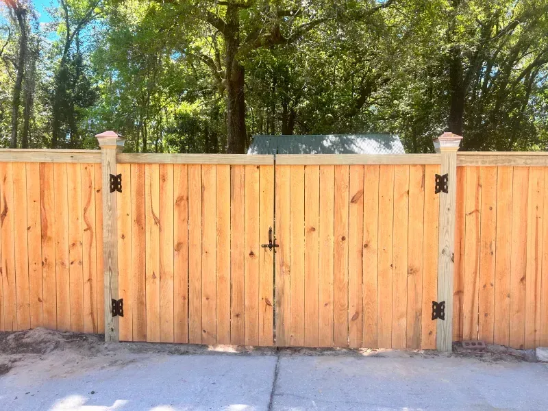 A wooden fence with a gate is sitting on top of a concrete driveway.