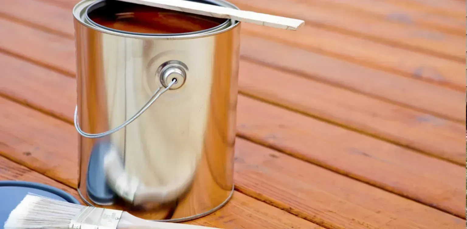 A can of paint and a brush on a wooden deck.