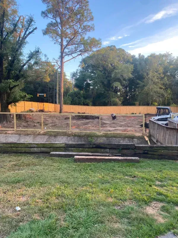 A wooden fence surrounds a grassy field with trees in the background.
