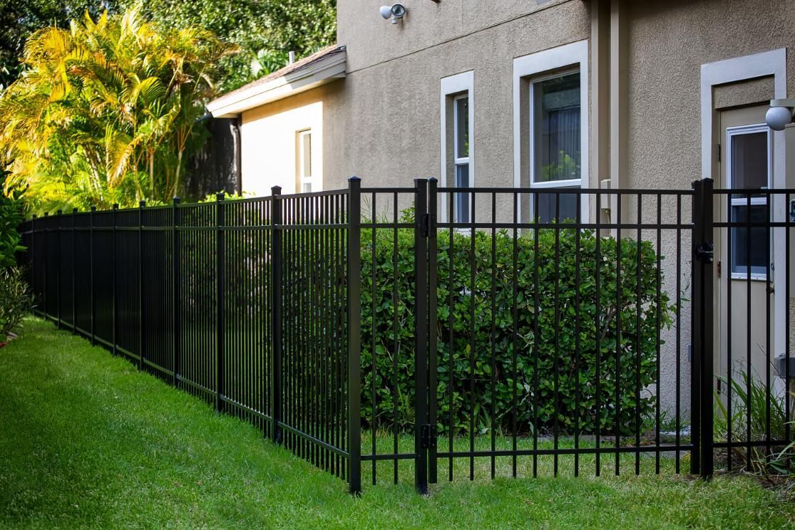 A black metal fence surrounds a lush green yard in front of a house.