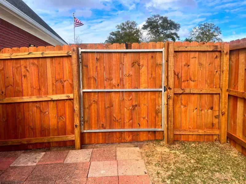 A wooden fence with a metal gate in the backyard of a house.
