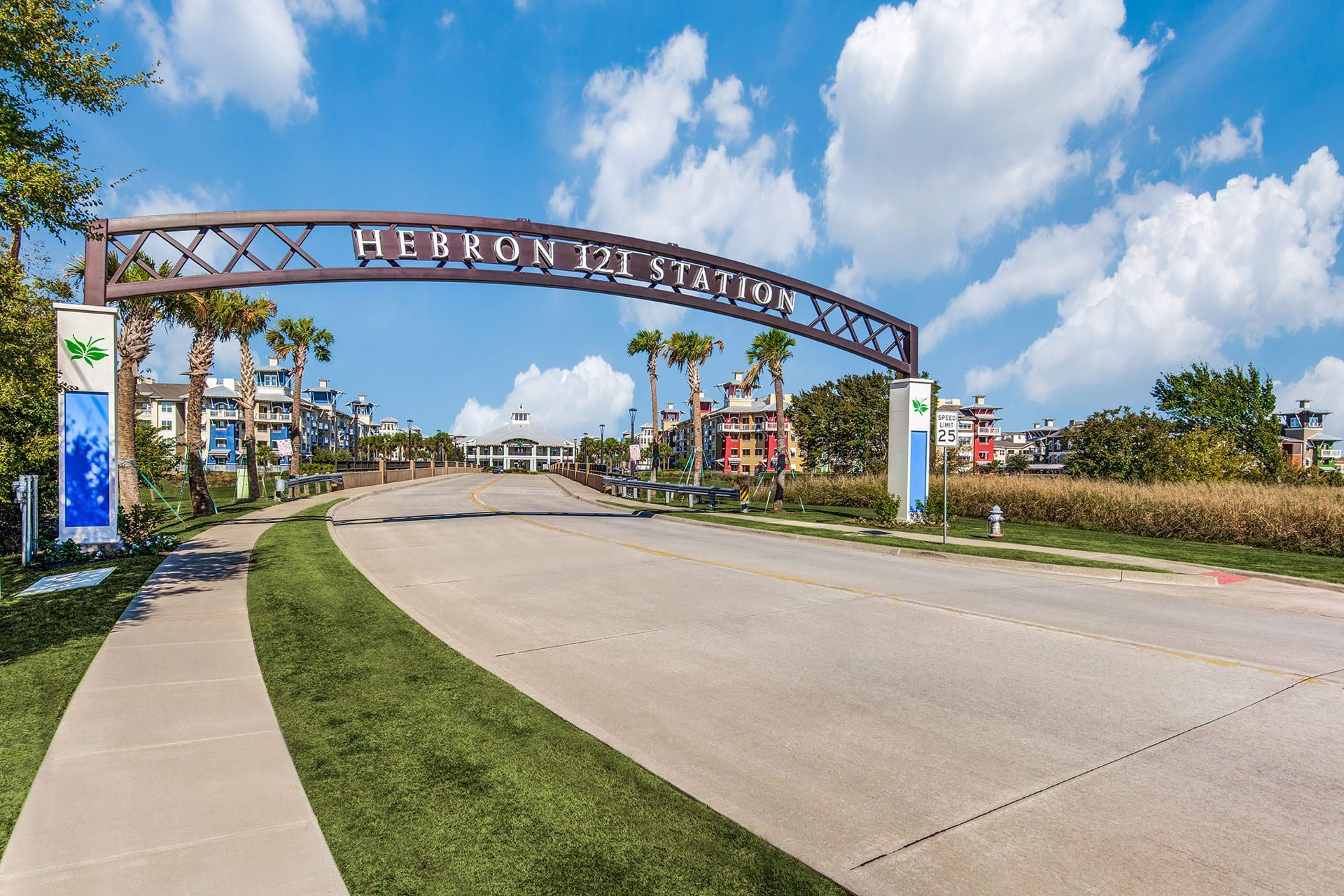 Entrance to Heron Bay Station, with an archway, sign, and roadway leading into a residential area.