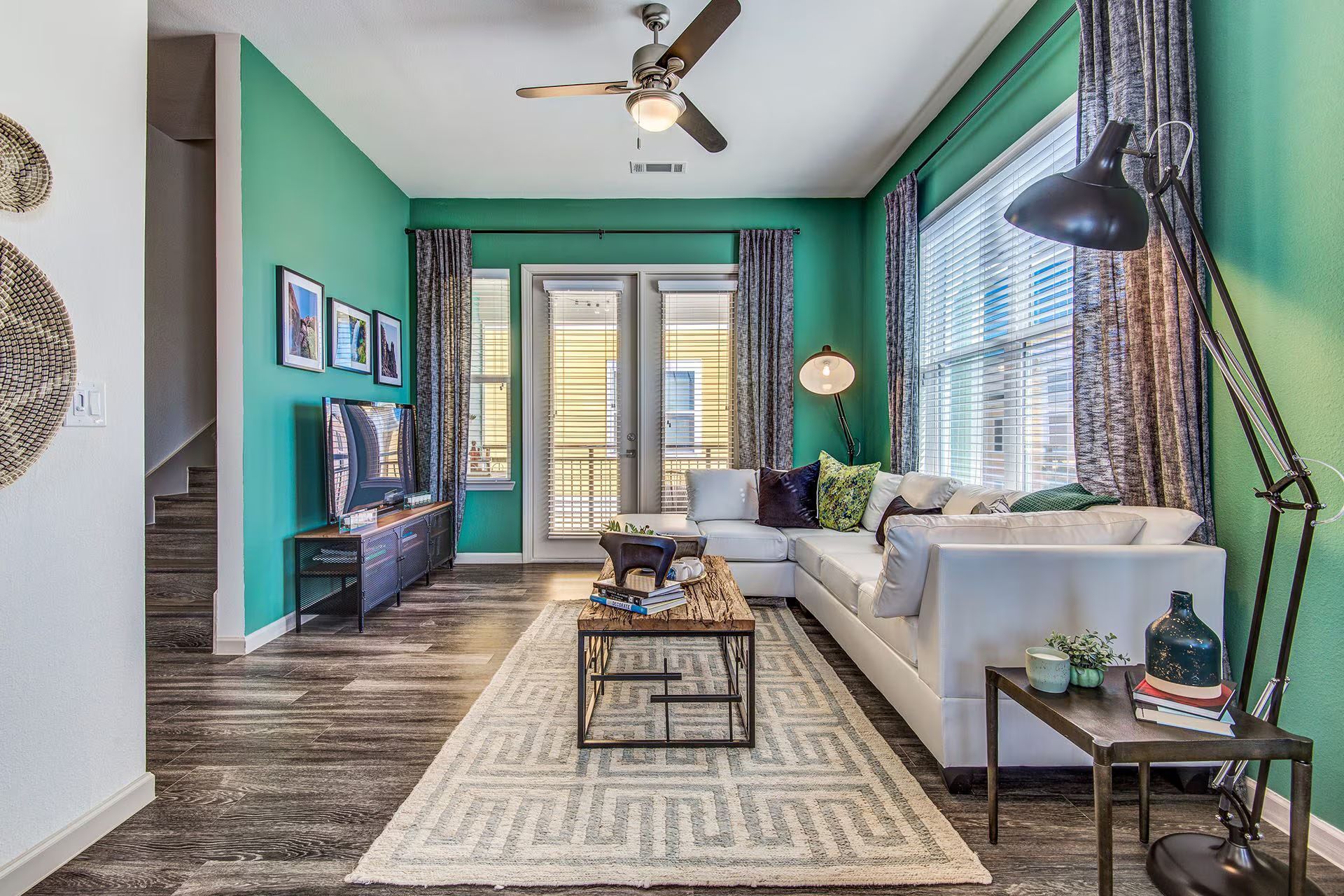 Living room with turquoise walls, white sectional sofa, balcony doors, and wood-look flooring.
