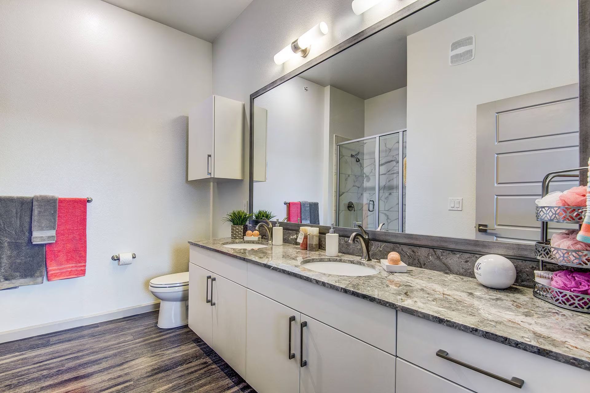 Bathroom with white cabinets, granite countertop, large mirror, and gray and red towels.