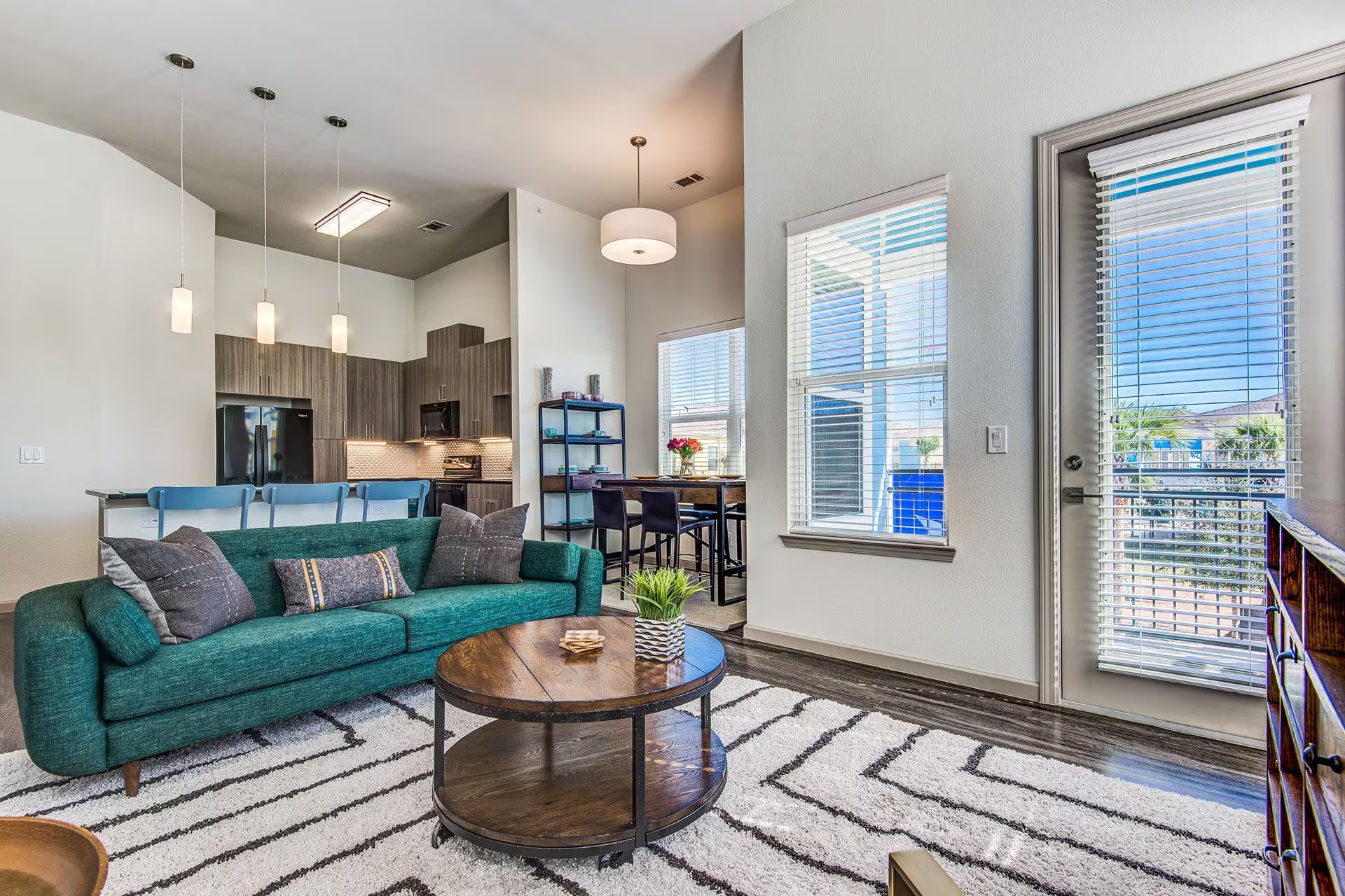 Modern living room with teal sofa, round coffee table, and kitchen in the background.